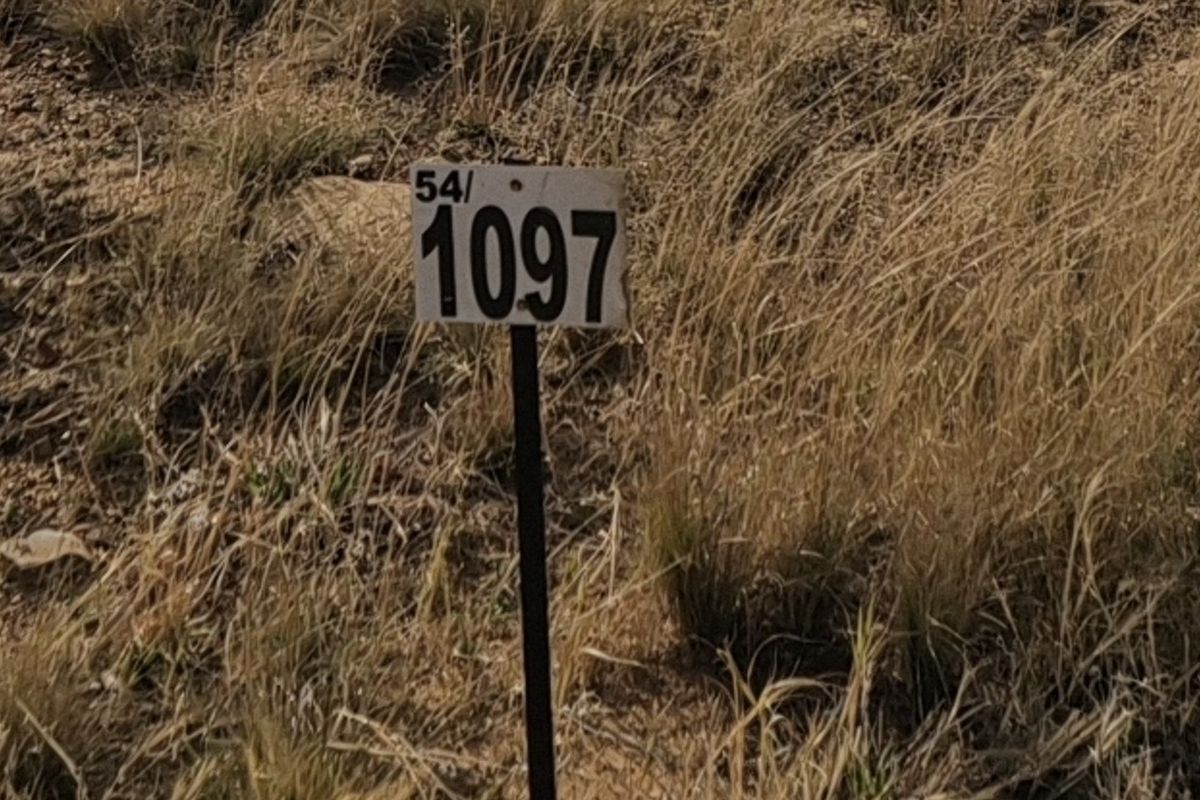 A close-up view of a property boundary marker stake indicating lot number 1097 on a vacant residential plot.