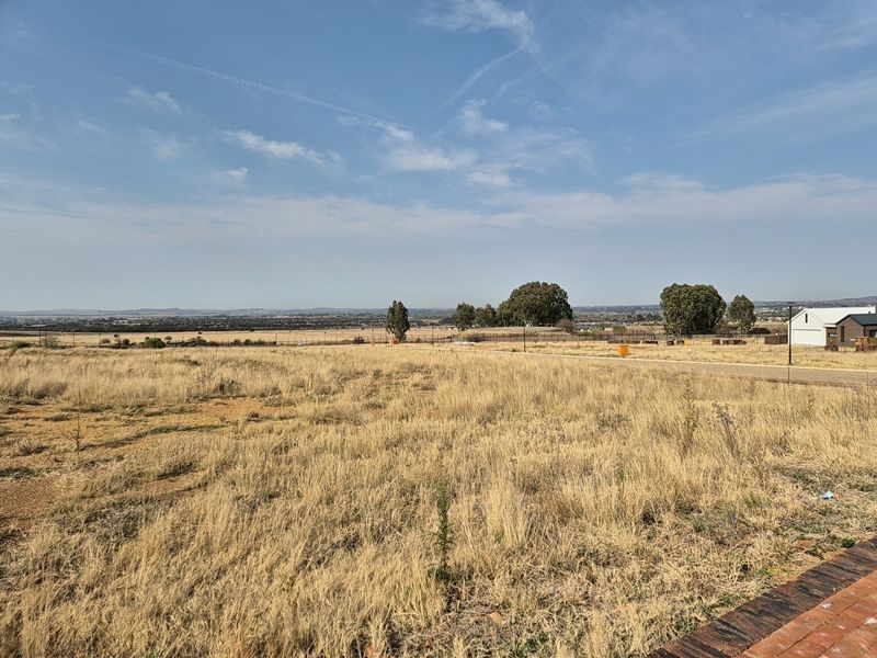 A wide-angle view of a vacant residential plot featuring dry grass and distant landscape views.