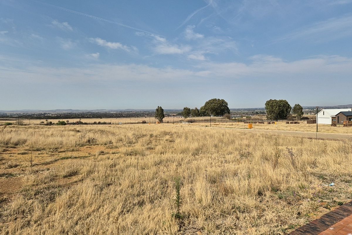 A wide-angle view of a vacant residential plot featuring dry grass and distant landscape views.