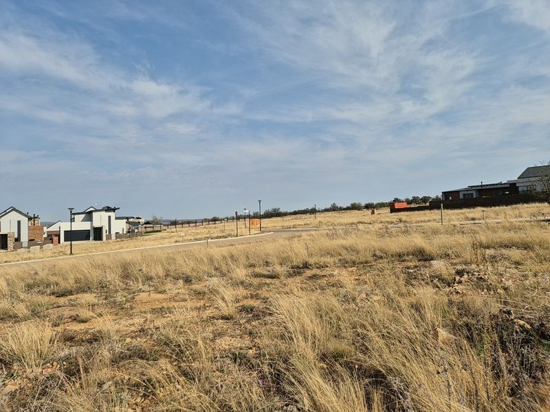 A view of a vacant residential plot in a developed estate, featuring established road infrastructure and surrounding modern residential homes.