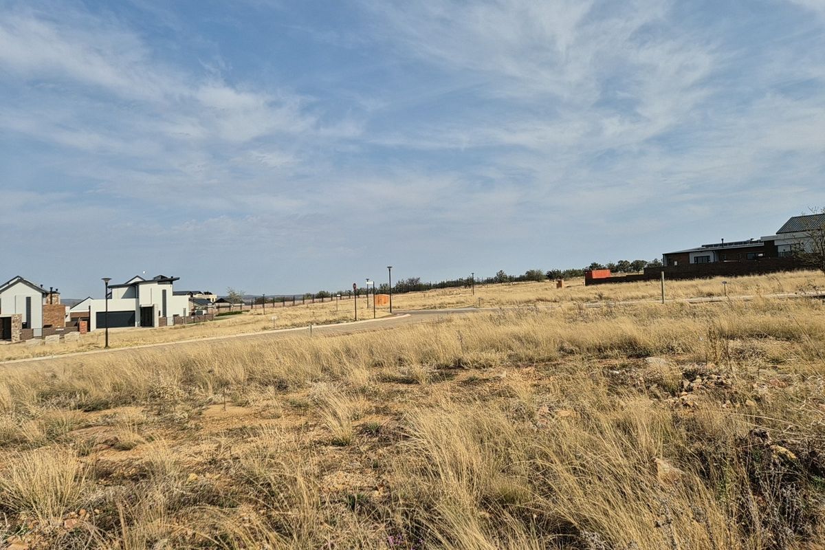 A view of a vacant residential plot in a developed estate, featuring established road infrastructure and surrounding modern residential homes.