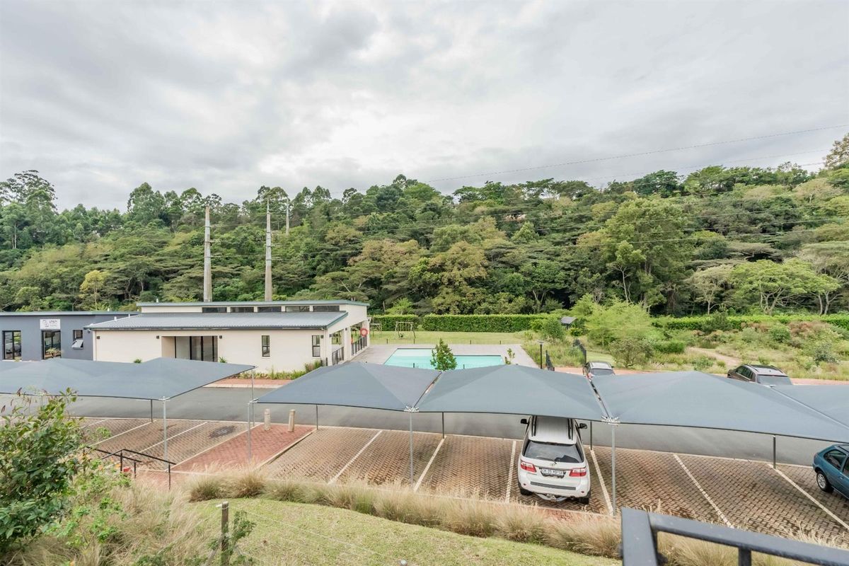 Elevated view of the apartment complex grounds, featuring covered parking bays, a communal swimming pool, and surrounding natural greenery.