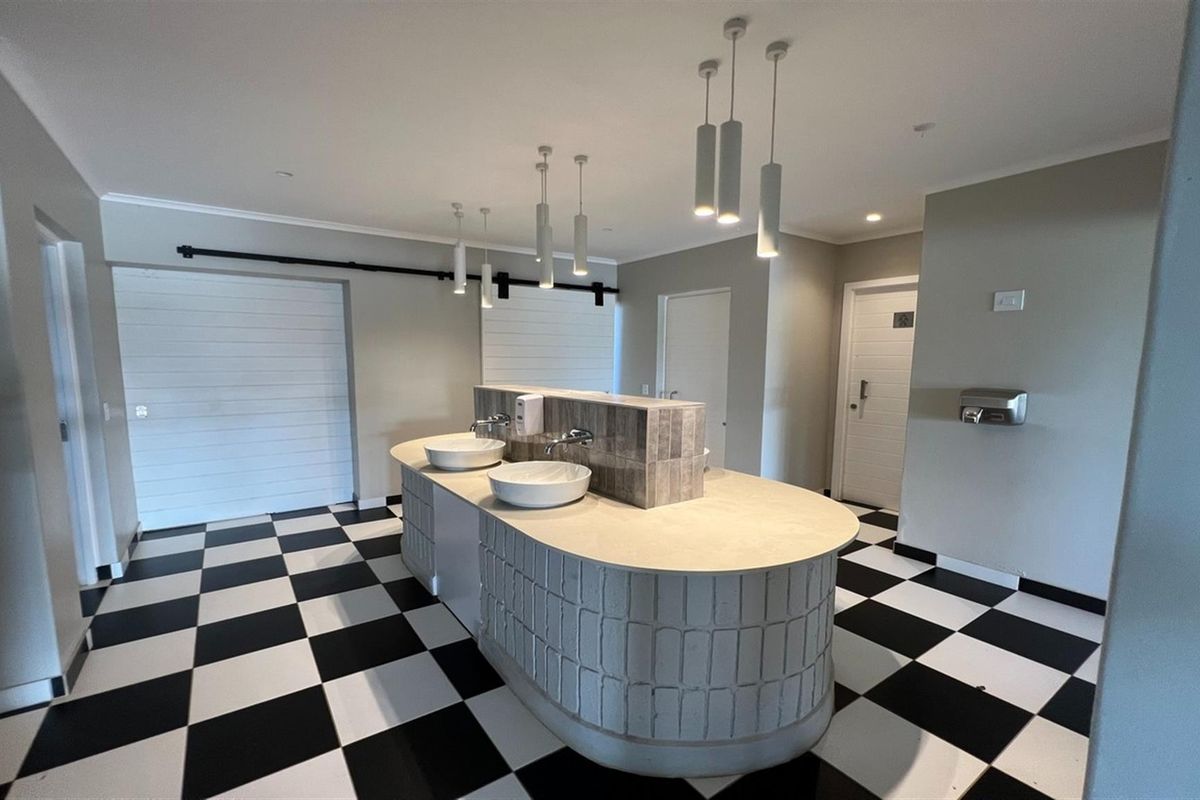 A modern bathroom facility featuring a central vanity island with dual vessel sinks, pendant lighting, and a distinctive black and white checkered floor.