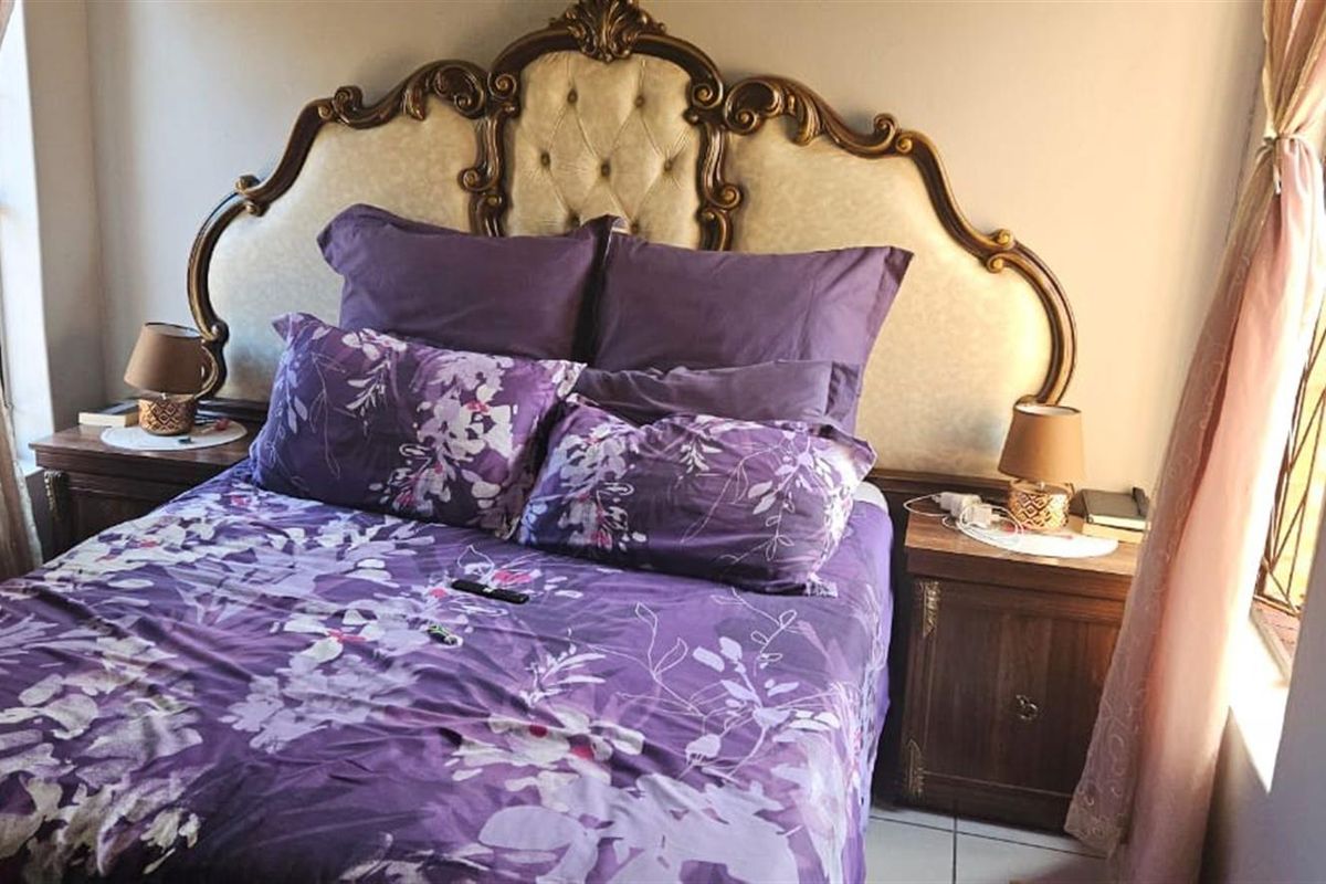 A cozy bedroom featuring tiled flooring and dual windows with curtains, providing natural light to the space.