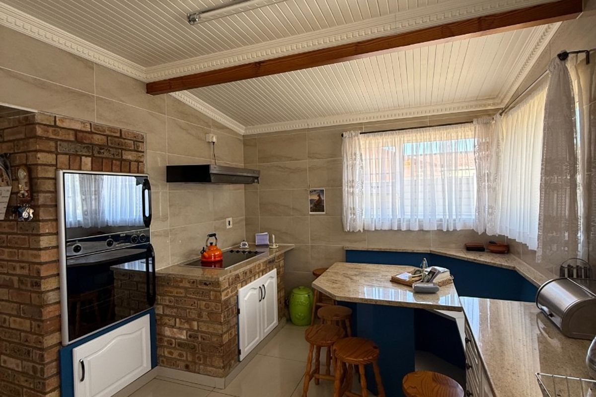 A rustic-style kitchen featuring exposed brick cabinetry, granite countertops, a built-in oven, and tiled flooring with a breakfast nook area.