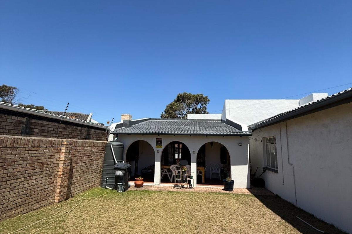 A rear view of the property featuring a covered patio with arched detailing, a brick boundary wall, and a private garden area.