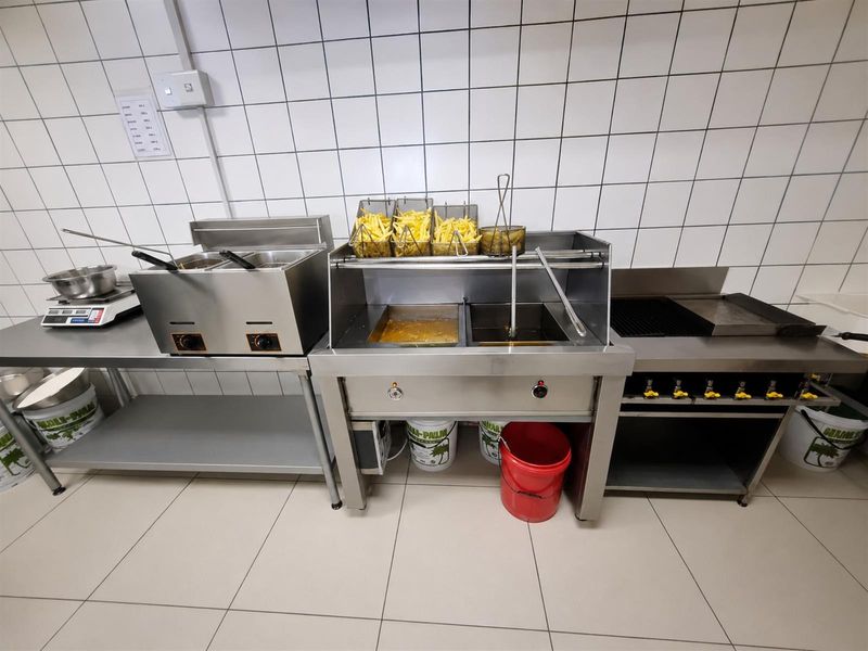 A functional commercial kitchen area featuring stainless steel deep fryers, a grill, and durable tiled wall and floor finishes.
