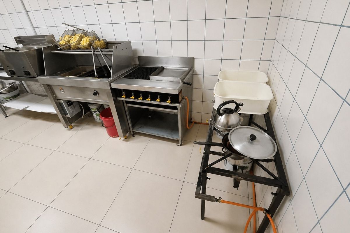 Commercial kitchen prep area featuring stainless steel deep fryers, a gas grill, and tiled wall finishes.