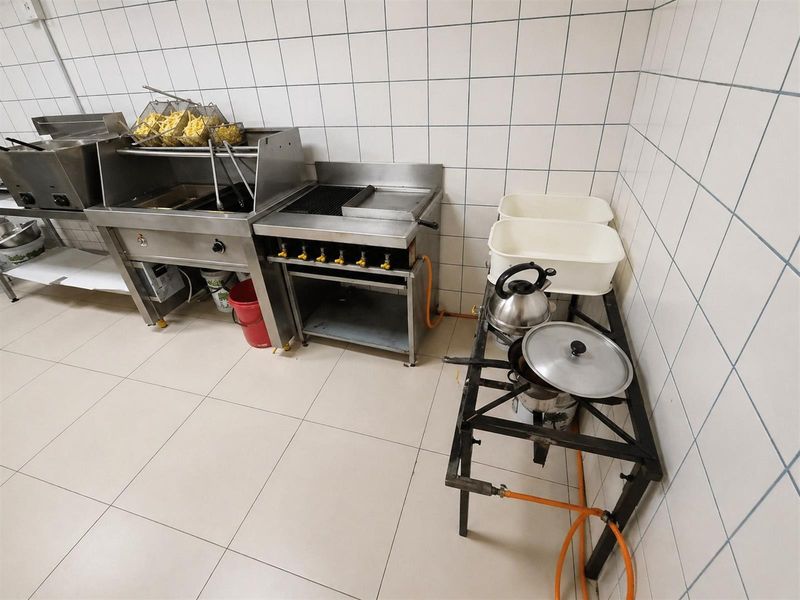 A functional commercial kitchen area featuring stainless steel deep fryers, a gas grill, and tiled wall finishes for easy maintenance.
