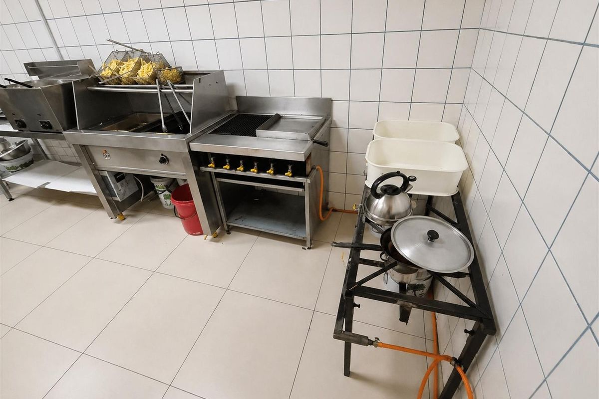 A functional commercial kitchen area featuring stainless steel deep fryers, a gas grill, and tiled wall finishes for easy maintenance.