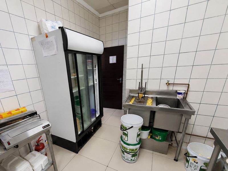 A functional commercial kitchen area featuring tiled walls, durable flooring, and a stainless steel double sink station.
