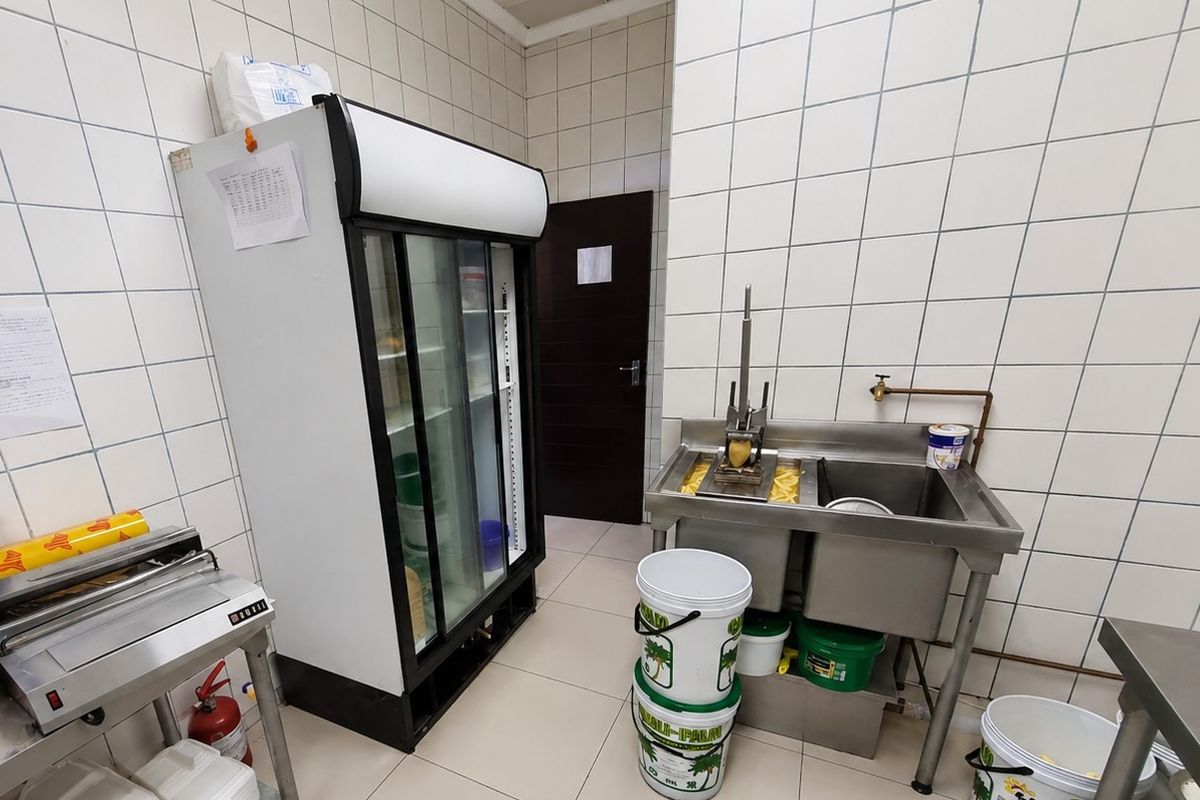 A functional commercial kitchen area featuring tiled walls, durable flooring, and a stainless steel double sink station.