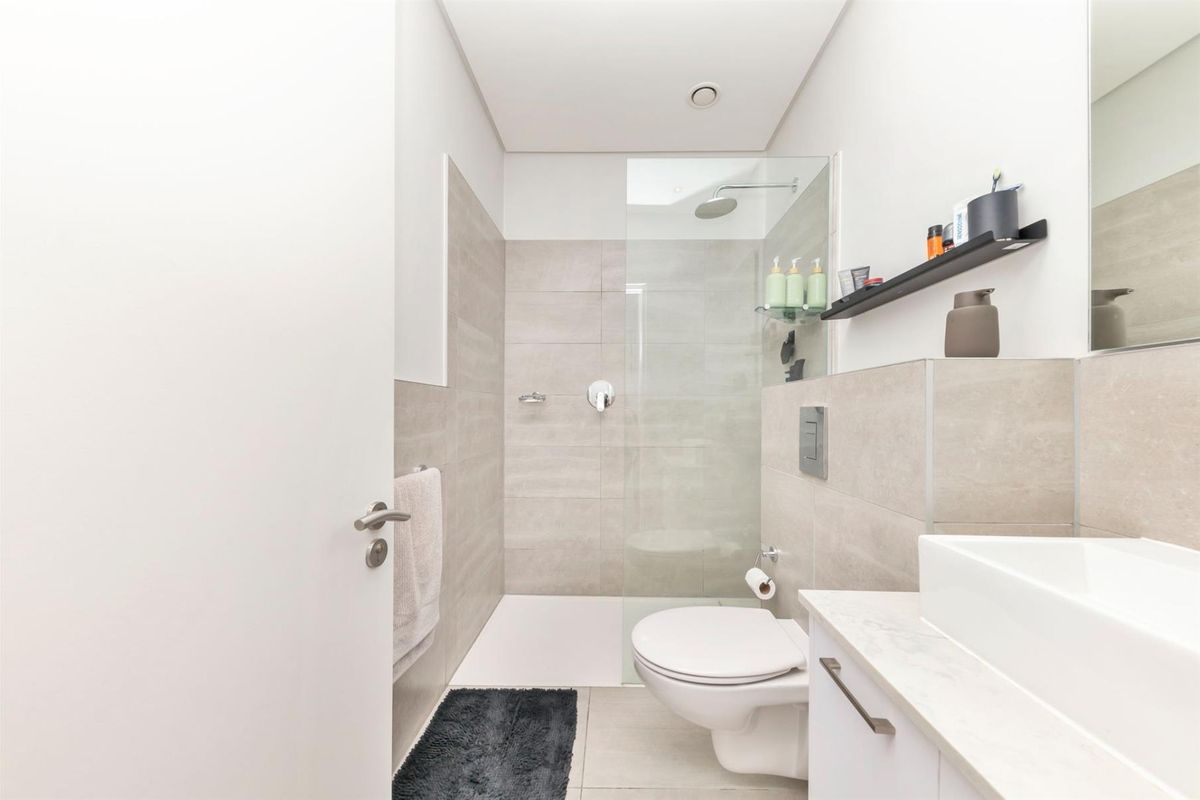 Modern bathroom featuring a walk-in shower with glass screen, wall-mounted toilet, and a sleek vanity with countertop basin.
