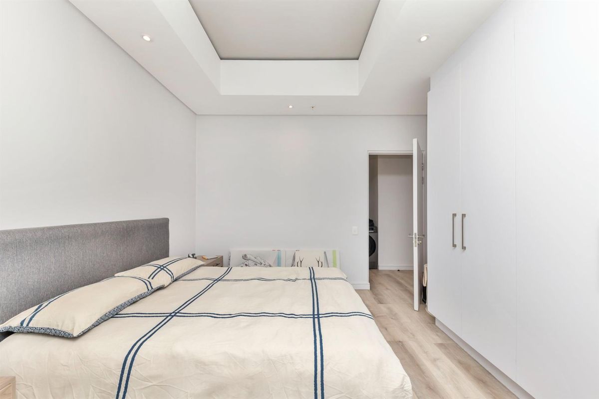 A modern bedroom featuring a recessed ceiling with downlights, light laminate flooring, and ample built-in cupboard storage.