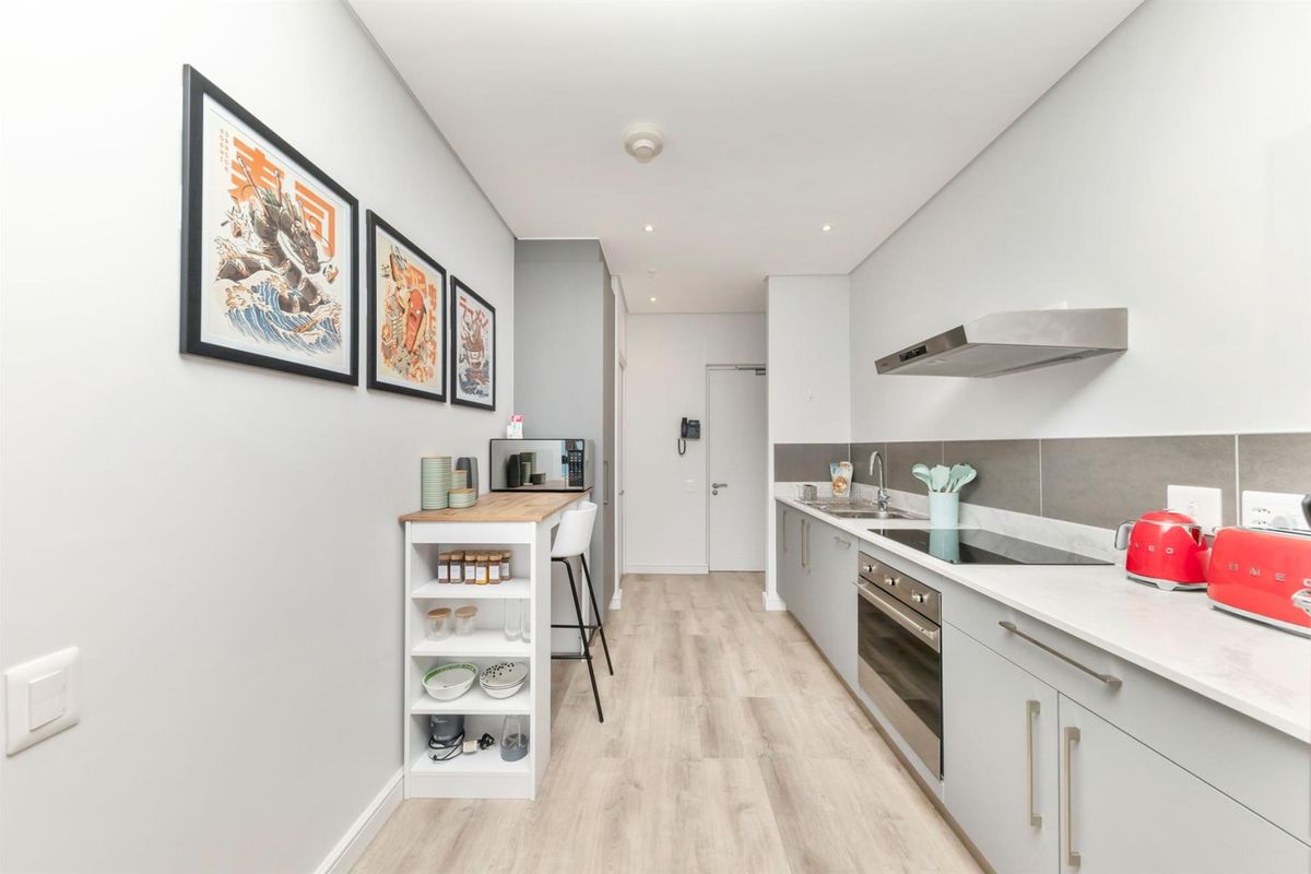 Modern galley-style kitchen featuring sleek grey cabinetry, stone countertops, integrated appliances, and a tiled splashback, offering a clean and functional workspace.