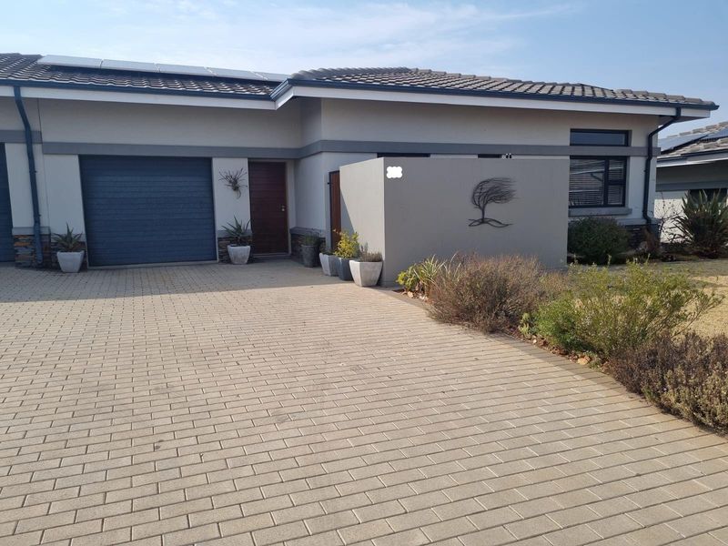 Front elevation of a modern house featuring a paved driveway, single garage, and a privacy wall with decorative metal art.