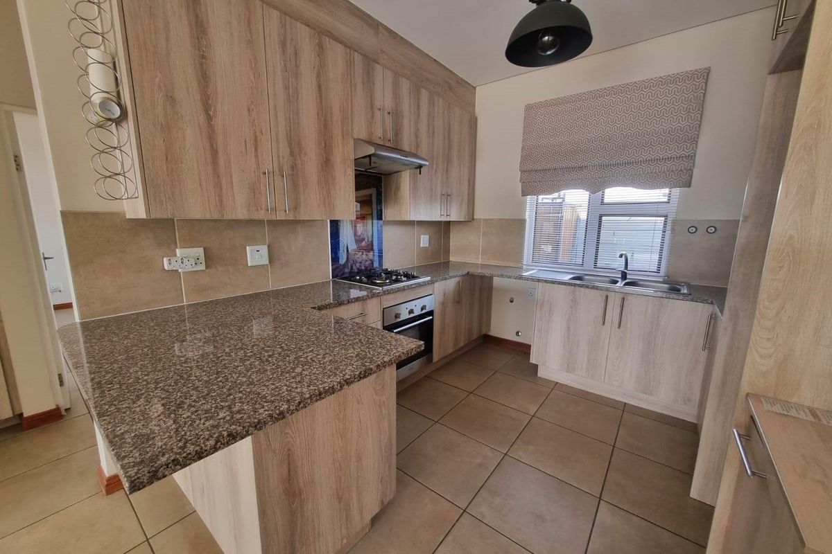 A well-maintained kitchen featuring wood-look cabinetry, granite countertops, a built-in oven with gas hob, and tiled flooring.