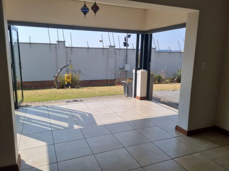 Covered patio area featuring tiled flooring and large folding glass doors opening onto a private garden with perimeter wall and electric fencing.