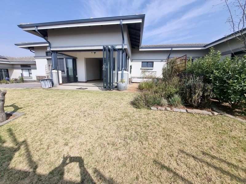 Rear view of the property featuring a landscaped garden, paved patio area, and modern bi-fold doors leading into the home.
