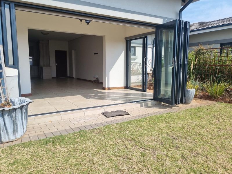 A seamless indoor-outdoor transition featuring modern bi-fold doors opening from a tiled patio onto a well-maintained garden lawn.