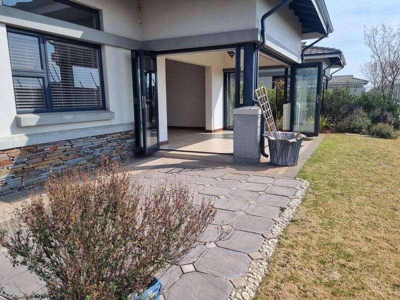 A covered patio area featuring stone cladding, bi-fold doors leading to the interior, and paved flooring, overlooking a landscaped garden.