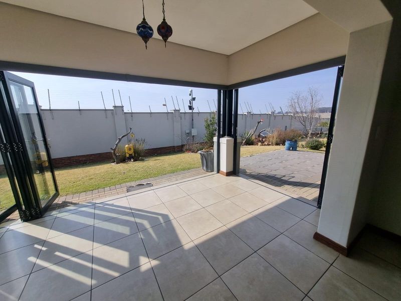 Covered patio area featuring large stacking doors that open onto a private garden with perimeter wall and electric fencing.