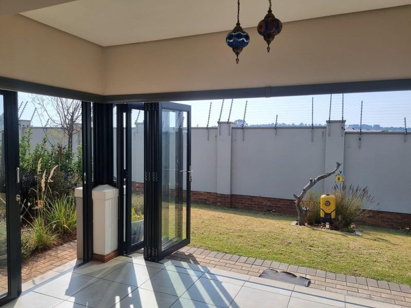 Covered patio area featuring modern stacking glass doors that open onto a private garden with perimeter wall and electric fencing.
