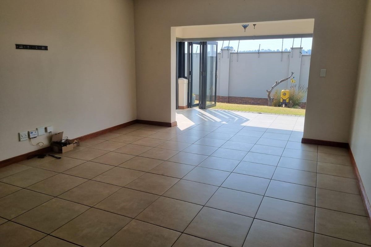 An empty living room featuring neutral tiled flooring and large stacking doors that open out to a private rear garden area.