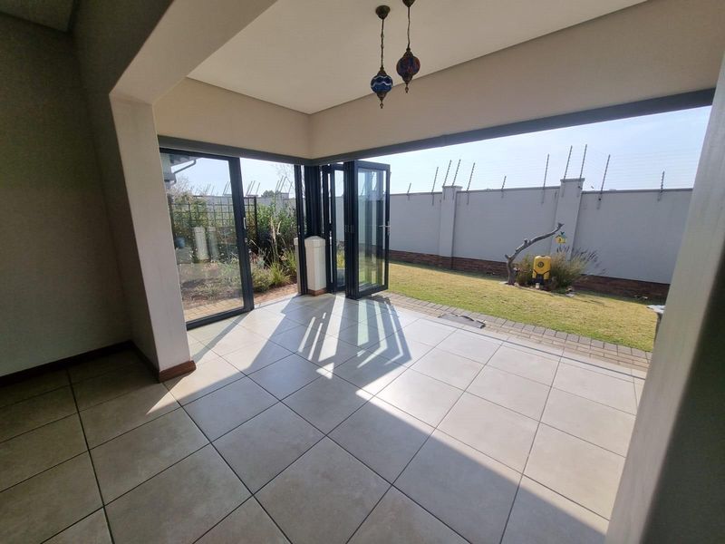 A spacious covered patio featuring large bi-fold glass doors that open onto a private garden area, perfect for indoor-outdoor entertaining.