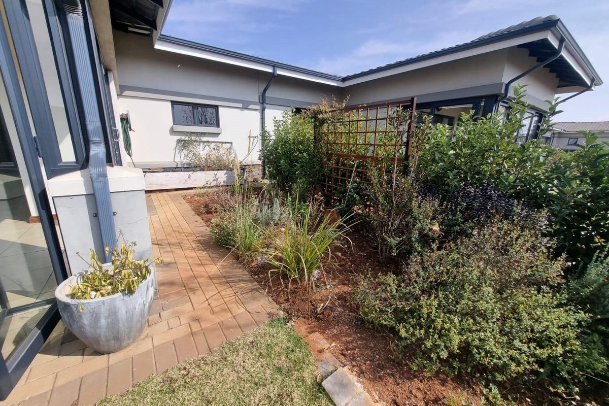 A well-maintained rear garden area featuring a paved walkway, established garden beds, and a decorative trellis against the exterior wall of the house.