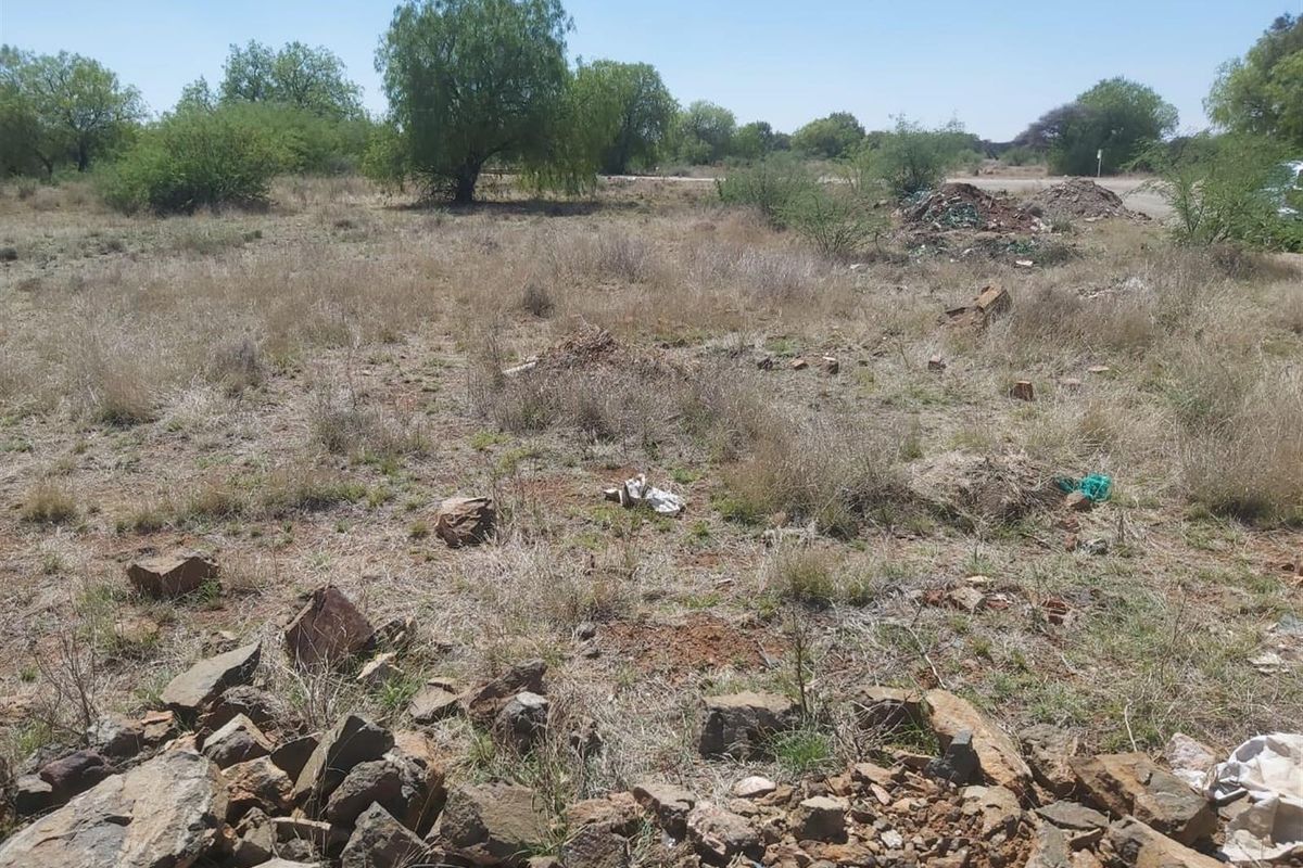 A view of a vacant residential plot featuring natural vegetation, rocky terrain, and scattered debris on the ground.