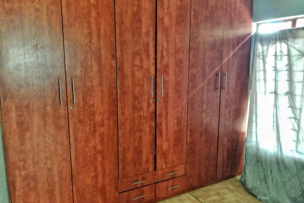 A bedroom featuring extensive floor-to-ceiling built-in wooden wardrobes with integrated drawers and modern metal handles, providing ample storage space.
