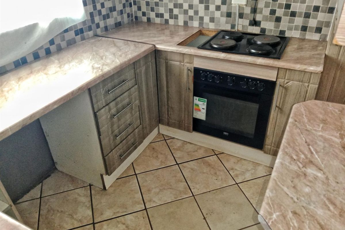 A functional kitchen corner featuring built-in cabinetry, a marble-effect laminate countertop, a fitted electric oven, and a four-plate hob with a tiled backsplash.
