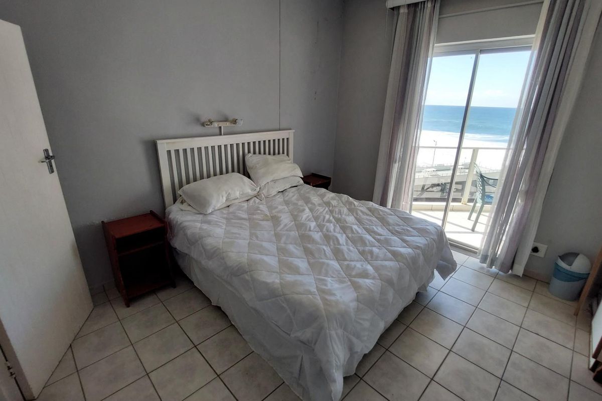 A bedroom featuring tiled flooring and a sliding glass door that opens onto a balcony with ocean views.