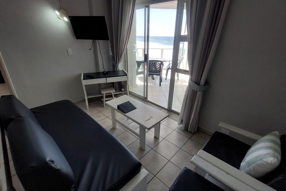 A compact living area featuring tiled flooring and sliding glass doors that open onto a balcony with ocean views.