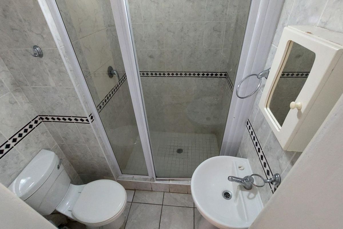 Compact bathroom featuring a tiled shower enclosure, pedestal basin, and toilet with neutral wall tiling and decorative border accents.