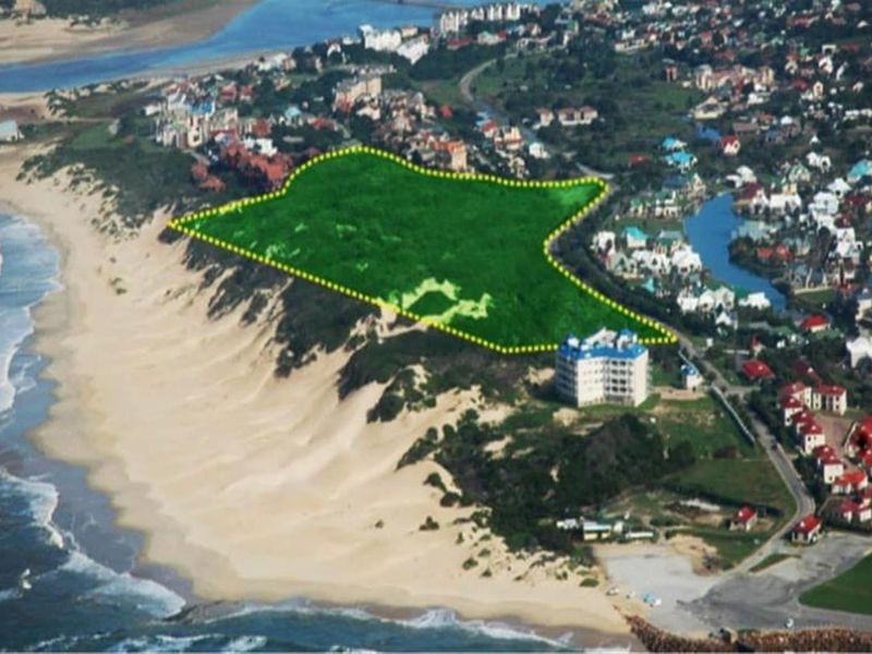 Aerial view of a vacant residential plot highlighted in green, situated along the coastline near a developed residential estate.