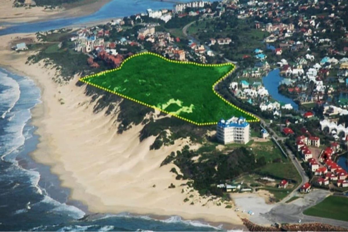 Aerial view of a vacant residential plot highlighted in green, situated along the coastline near a developed residential estate.