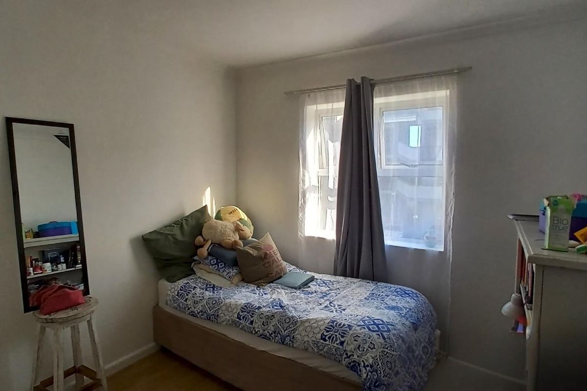 A functional bedroom featuring neutral walls, laminate flooring, and a window providing natural light.