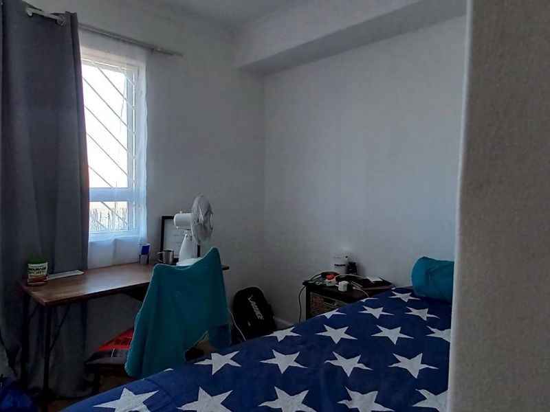 A functional bedroom featuring a window with security bars, providing natural light and a view of the exterior.