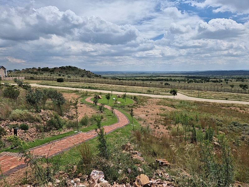 Expansive view of the surrounding landscape featuring a brick paved pathway, manicured garden elements, and secure perimeter fencing.