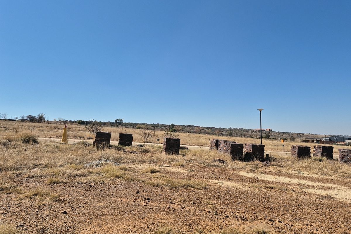 A vacant residential plot featuring dry grass, open terrain, and existing boundary markers under a clear blue sky.