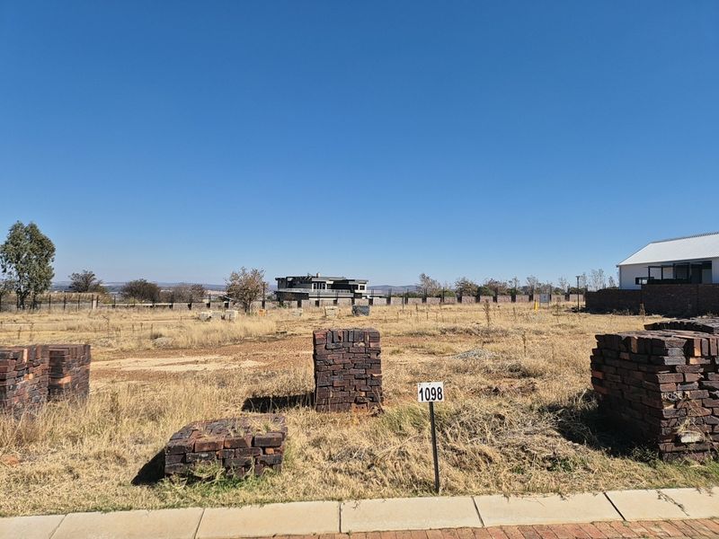 A vacant residential plot of land featuring dry grass, boundary fencing, and stacked construction bricks, ready for development.