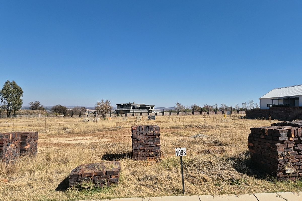 A vacant residential plot of land featuring dry grass, boundary fencing, and stacked construction bricks, ready for development.