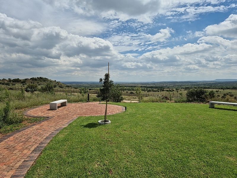 A scenic view overlooking a vast landscape, featuring a well-maintained lawn and a brick-paved patio area.