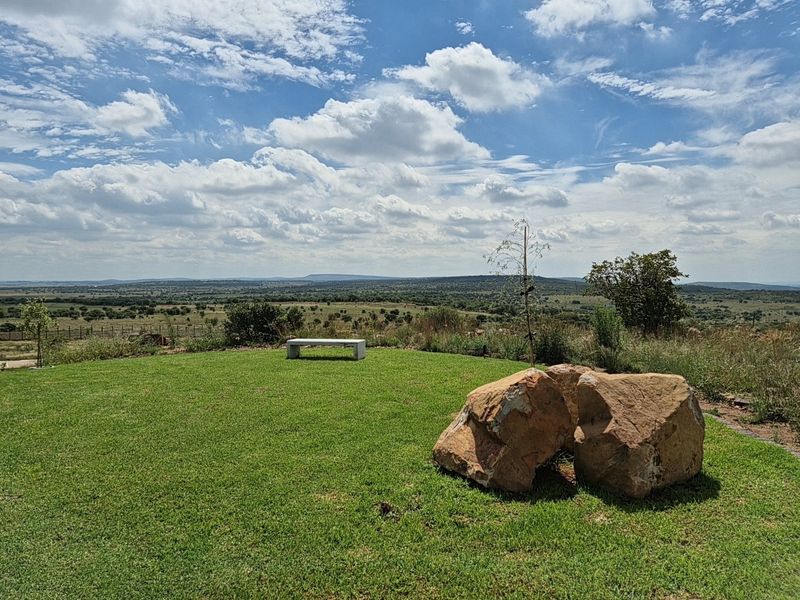 A scenic view overlooking expansive natural landscape, featuring a well-maintained lawn, large decorative boulders, and distant horizon vistas.
