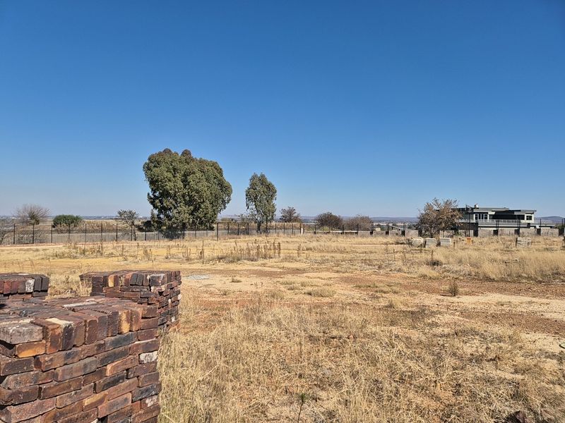 A vacant residential plot featuring dry grass, perimeter fencing, and clear views of the surrounding landscape.