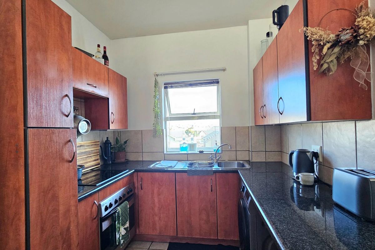 A compact kitchen featuring wood-finish cabinetry, dark granite countertops, a built-in oven and hob, and a stainless steel sink.