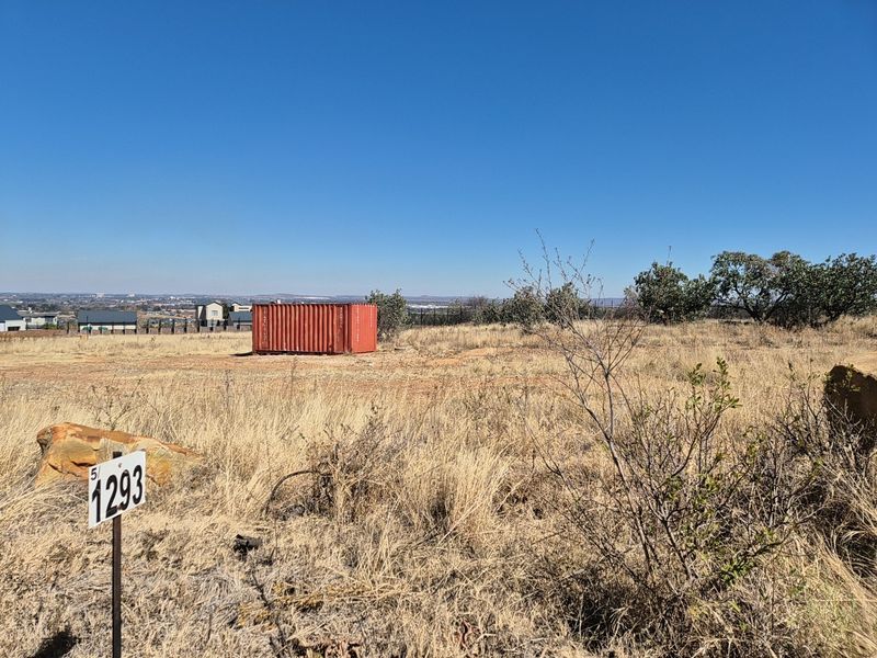 A view of a vacant residential plot featuring dry grass, natural terrain, and a property boundary marker.