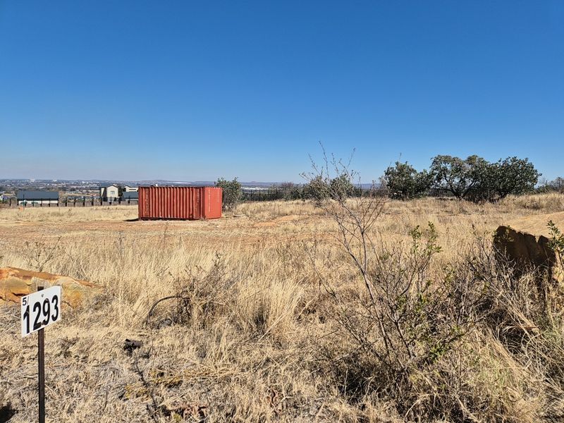 A view of a vacant residential plot featuring dry grass, natural vegetation, and a boundary marker post.
